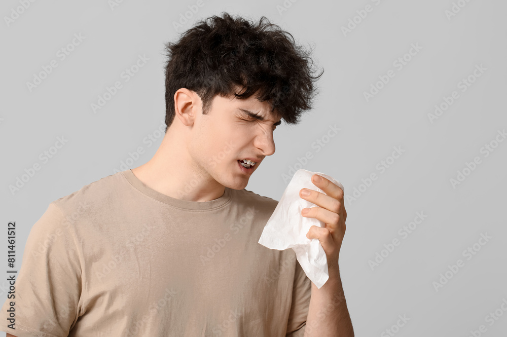 Young man with runny nose on grey background. Allergy concept Young man with runny nose on grey background. Allergy concept
