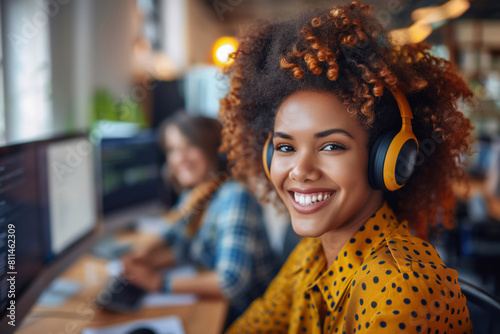 Smiling African American woman with headphones working in a busy office environment, providing customer support