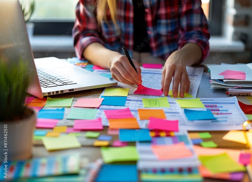 Close up of hands making a plan on a desk with sticky notes, an office worker or businesswoman working at a table near a computer and documents using modern tech equipment for project management. Close up of hands making a plan on a desk with sticky notes, an office worker or businesswoman working at a table near a computer and documents using modern tech equipment for project management.