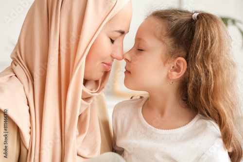 Little girl with her Muslim mother touching noses at home, closeup photo