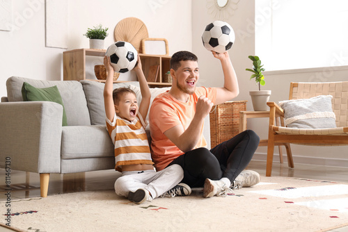 Young man and his little son cheering for football team with soccer balls at home photo