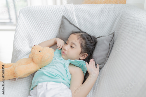 cute asian children stretching on white sofa, she sleepy and lazy in the morning, she hug a bear doll, child health promotion