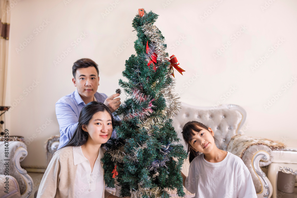 A family of three is decorating a Christmas tree A family of three is decorating a Christmas tree