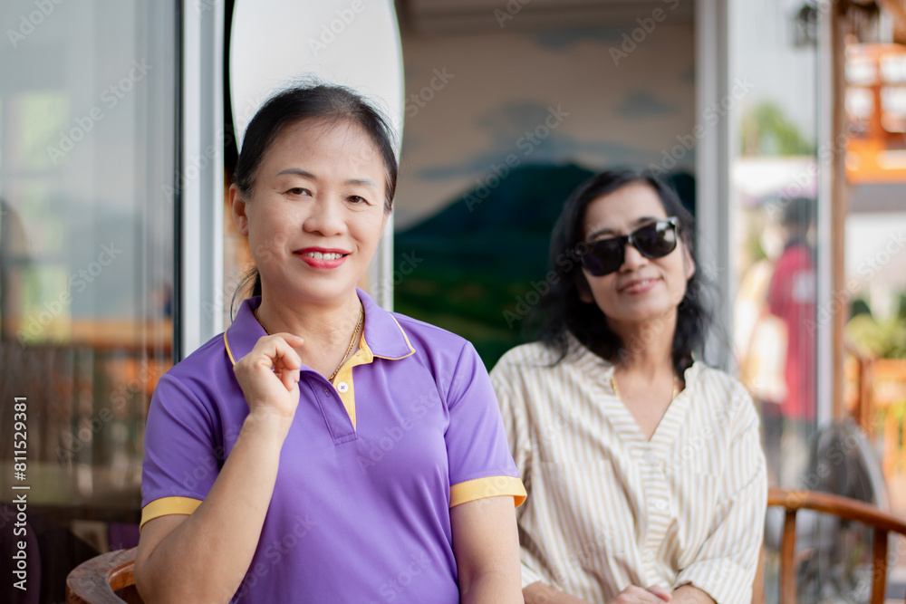 Fototapeta premium Asian middle-aged woman sitting with her friend in front of glass door of her house.