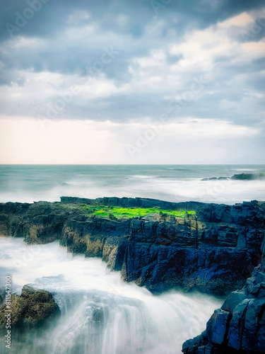 Long exposure of sea waves hitting rocks on a cloudy day