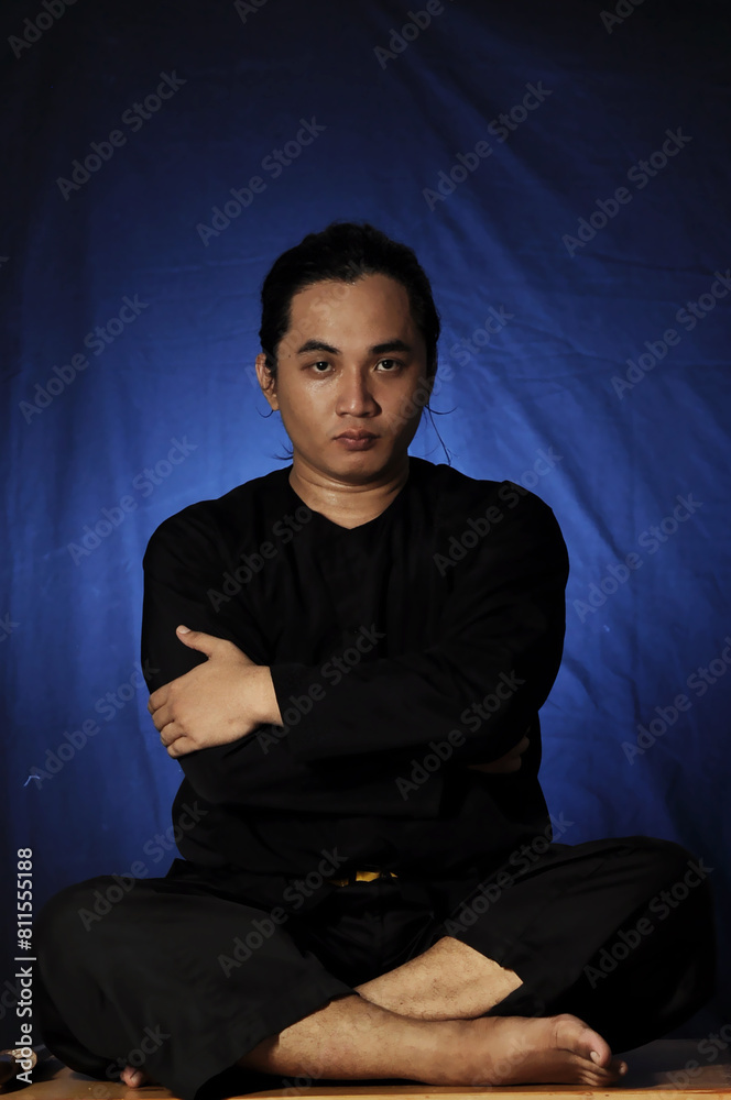 close-up of an Asian man in a pencak silat uniform holding an alert sitting pose close-up of an Asian man in a pencak silat uniform holding an alert sitting pose