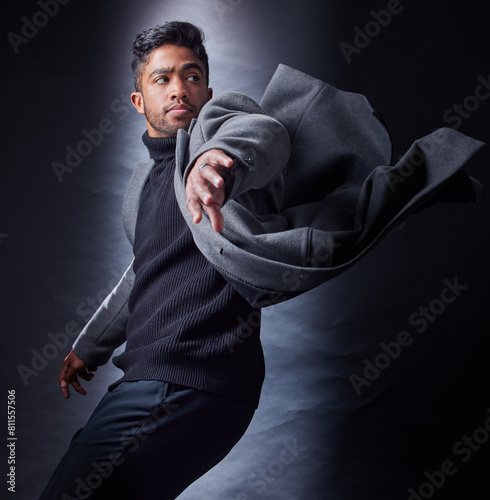 Man, serious and fashion or dark studio, spy and coat with wind for escape and looking. Classy, semi formal and outfit on black background, male model and Indian person with trendy winter clothes photo