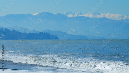 Snow Mountains In Haze Across The Bay At A Great Distance. Sunrise At Beach With Snowy Mountains. Real time.