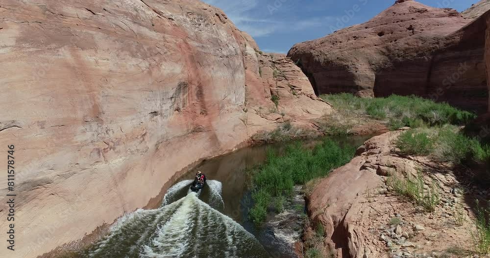 Jet ski slowly traveling through red, rocky, desert river - drone shot Jet ski slowly traveling through red, rocky, desert river - drone shot