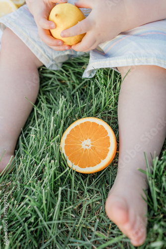 Child holding a lemon and half an orange laying in the grass photo