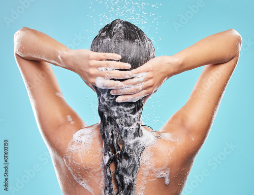 Back, shower and woman with skincare, foam and hair care on blue studio background. Rear view, person or model with water drops, shampoo or cleaning with liquid, grooming routine or wet with wellness