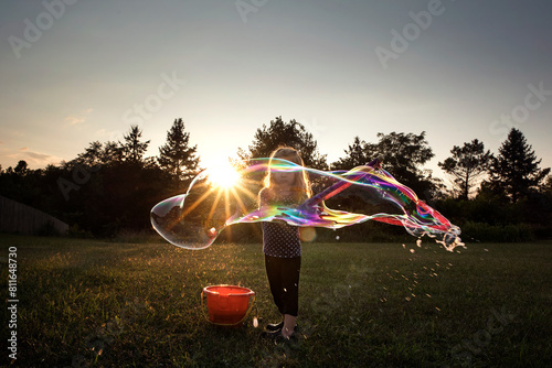 Little girl blowing giant colorful bubble in grassy field at sunset photo