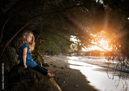 Little girl with long blonde curls looking at water under sunny sky