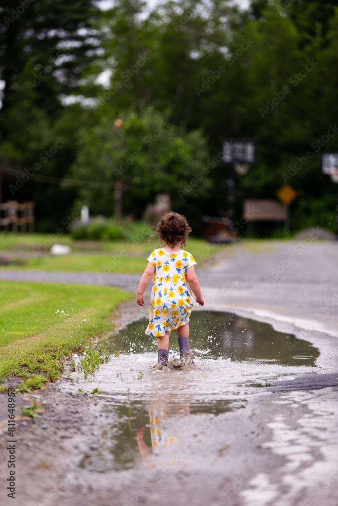 Toddler Girl in Dress and Rainboots Splashing in Puddle Toddler Girl in Dress and Rainboots Splashing in Puddle
