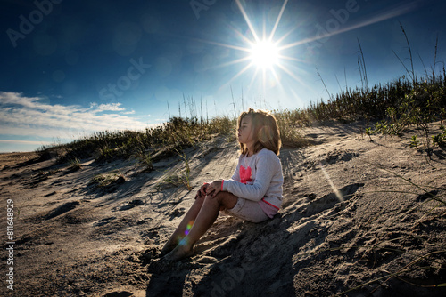 Young girl sitting and thinking on sand dune under sunny blue sky photo