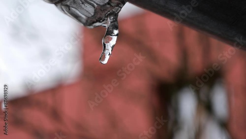 Water drops falling from melting icicle on gutter in early spring