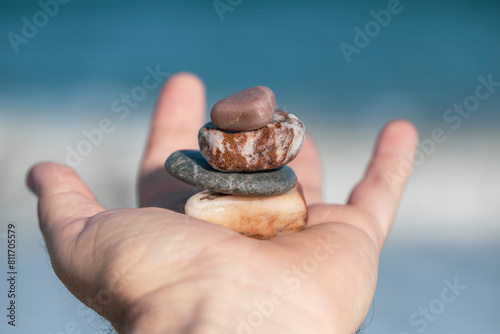 Open hand with a stack of four pebbles of different colors on a beach in flat daylight that convey zen calm