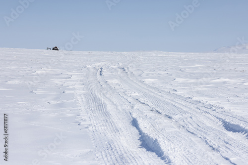 Winter road in the tundra. View of a winter road in the snowy tundra in the Arctic. An abandoned house in the distance. Desert winter arctic landscape. White silence. Tread marks in the snow. photo
