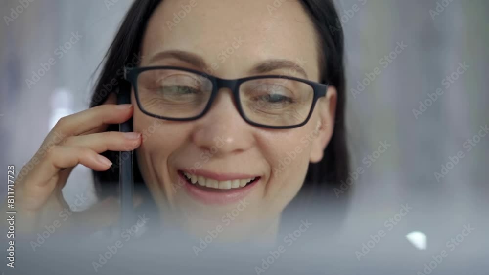 Cheerful smiling woman with glasses using a mobile phone, blurred background. Lifestyle and business concepts Cheerful smiling woman with glasses using a mobile phone, blurred background. Lifestyle and business concepts