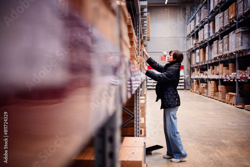 Young woman in motion, reaching out to a shelf in a warehouse. The blur effect emphasizes her swift movement as she navigates through the vast rows of stock. 