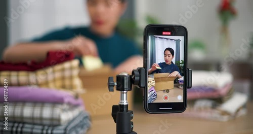 Footage selective focus shot, Young asian woman business owner selling clothes live streaming on mobile phone and packed clothes into box for a customer ,Online Shopping