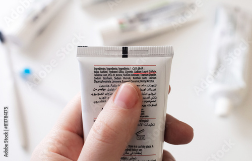 Dangerous toothpaste ingredient SLS, sodium laureth sulfate. Checking the composition of toothpaste with a magnifying glass against the background of many tubes