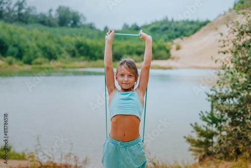 Young girl stretching with a yoga strap outdoors by a river, demonstrating flexibility and exercise