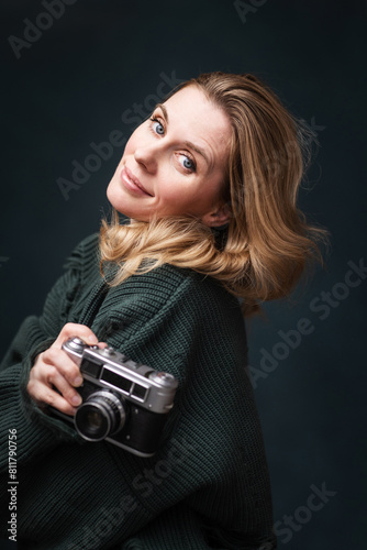 pretty, young woman photographer on a dark background with a camera in her hands.