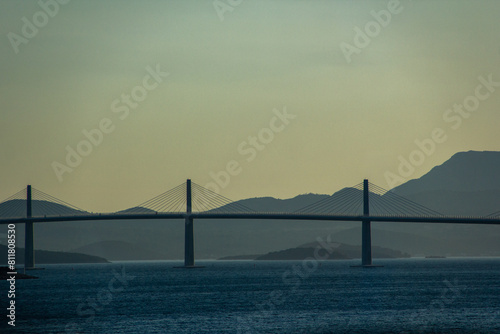 Suspension bridge across the sea strait against the backdrop of mountains and islands in the evening twilight