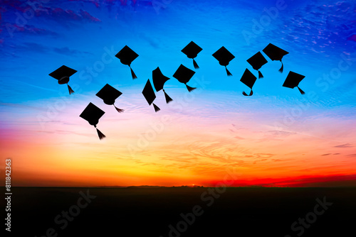 Silhouettes of graduation caps flying upward against bright watercolor sunset sky. Bright graduation ceremony background