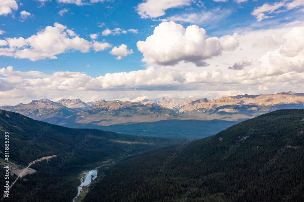 High mountain peaks covered snow and forest below. Cumulus clouds, blue sky. Mountain landscape. High mountain peaks covered snow and forest below. Cumulus clouds, blue sky. Mountain landscape.
