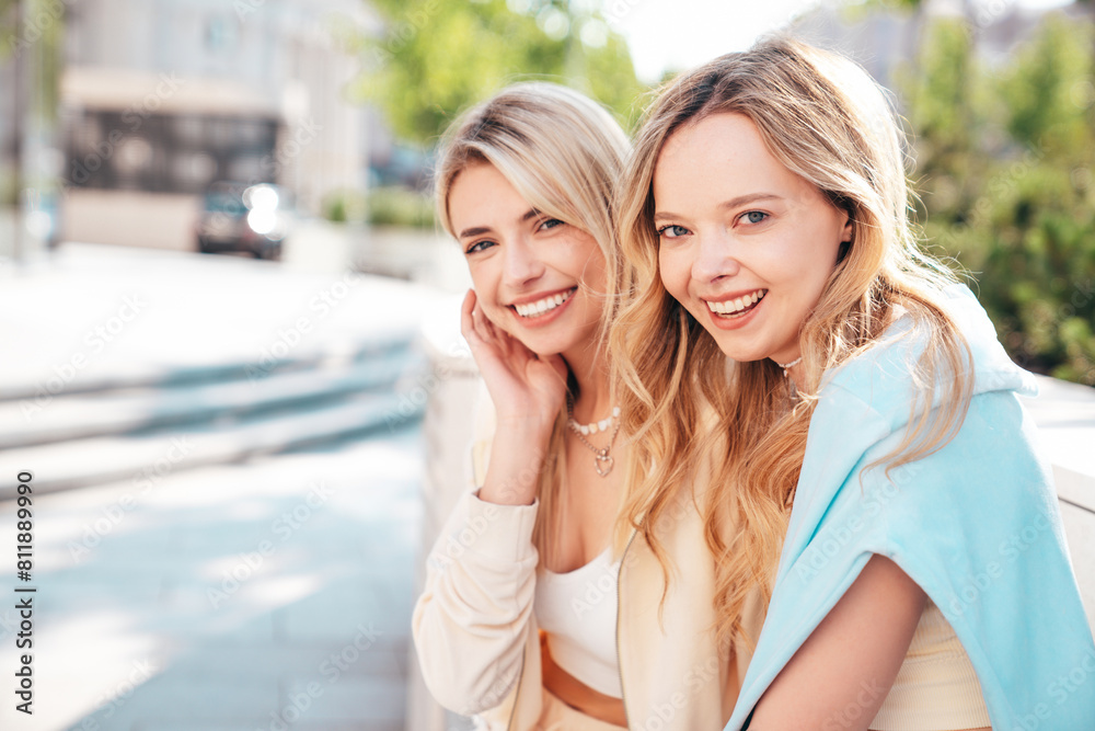 Fototapeta premium Two young beautiful smiling blond hipster female in trendy summer clothes. Sexy carefree women posing on street background. Positive models having fun, hugging at sunset. Cheerful and happy