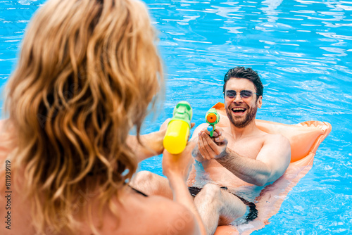 Merry young man enjoying the water pistol battle with a woman at the poolside. Summer vacation and leisure activity concept