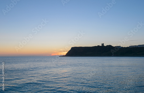 The headland at the southern end of North Bay in Scarborough, North Yorkshire, UK, backlit at dawn sunrise. Scarborough Castle is silhouetted on the headland. photo