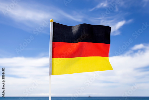 German flag fluttering in the wind in front of blue sky with white clouds and sea