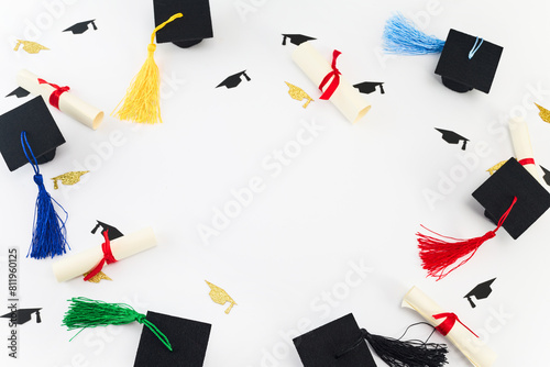 Graduation Celebration Theme. Top view of miniature graduation caps and diplomas with colorful tassels on white.