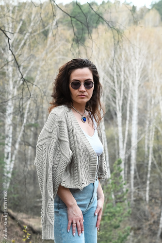Girl with glasses grey knitted jacket on a forest background