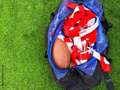 Flag Football Equipment on Green Turf. A large athletic duffel bag is filled with equipment for flag football play. Red and blue flags and a football fill the bag. Green turf football field background