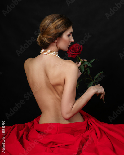 A naked girl is sitting in a red cloth and sniffing a rose