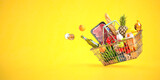Shopping basket full of grocery products, food and drink on yellow background.