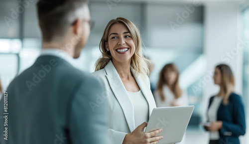 A smiling businesswoman standing in front of a group with her team holding a laptop and talking to each other