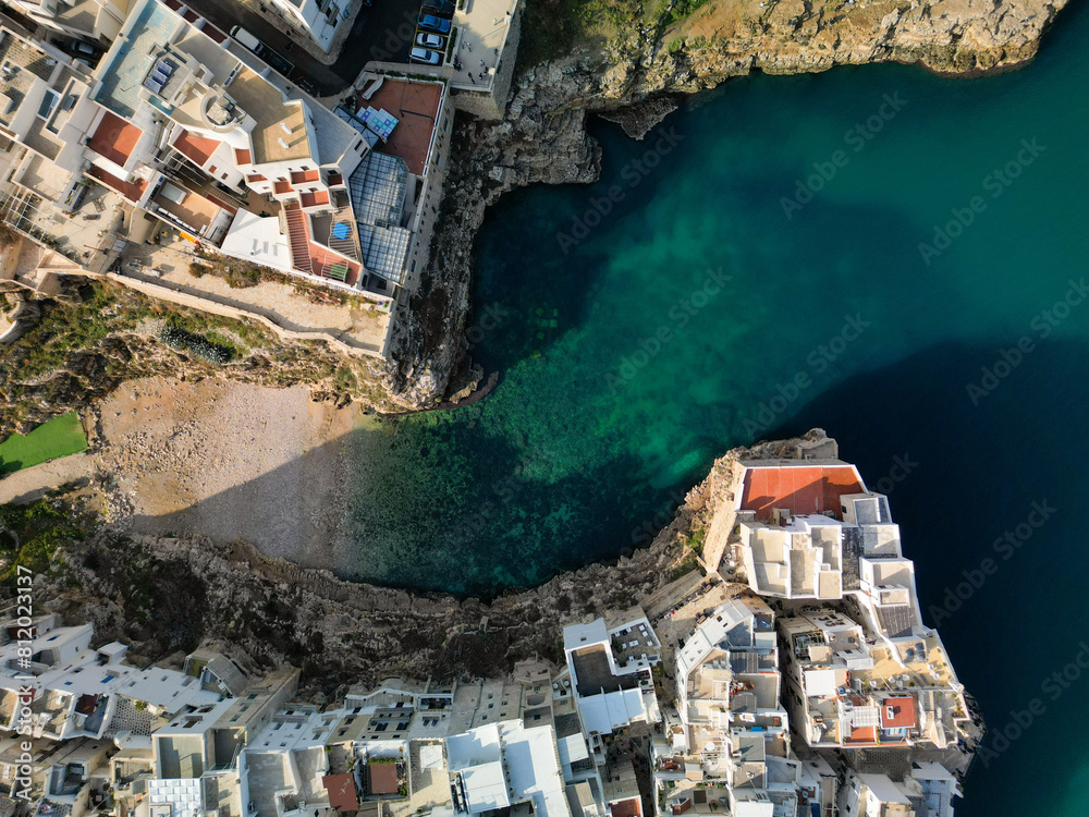 Aerial view of Polignano a Mare, a colorful village built next to a cliff and near the beach with turquoise water. Top-down drone photo taken in Puglia, near Bari, Italy. 