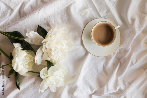 Fototapeta Naklejka Na Ścianę i Meble -  Morning coffee and peony flowers in bed. A tranquil morning routine with a cup of coffee amidst fresh white peonies on a soft linen textile background, conveying a sense of calm, serene, slow living.