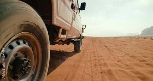 Closeup wheel of Off-road car tour in Wadi Rum Desert in Jordan. Adventures in Landmark Sand Valley of the Moon - tourist site in Middle East. 4K low angle view gimbal shot in slow motion photo