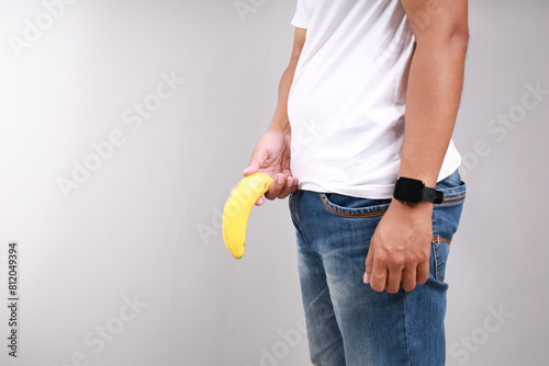 Impotence and men's health. A man in blue jeans, legs apart, holds a limp banana near the genitals. white background. Close up. Copy space