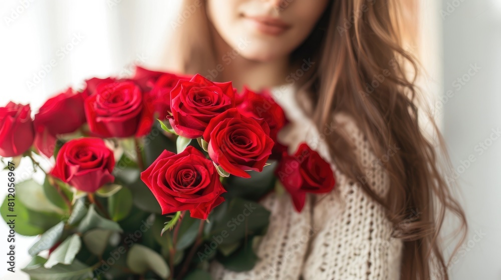 A close up shot captures a woman delicately cradling a luxurious bouquet of vibrant red roses against a light background A close up shot captures a woman delicately cradling a luxurious bouquet of vibrant red roses against a light background