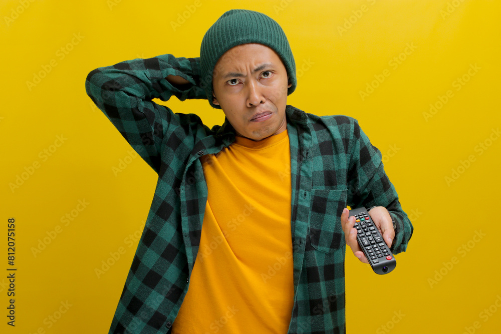 Unhappy Asian man, dressed in beanie hat and casual shirt, touches his head while holding a TV remote control, feeling disappointed and sad as he watches his favorite team lose in a sports game match Unhappy Asian man, dressed in beanie hat and casual shirt, touches his head while holding a TV remote control, feeling disappointed and sad as he watches his favorite team lose in a sports game match