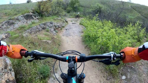 Two cyclists ride on a difficult rocky trail on mountain bikes. First-person view.