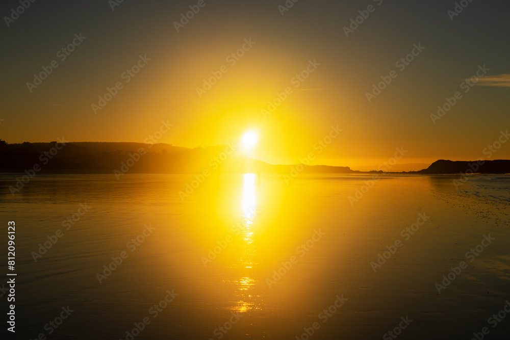 Sous un ciel teinté de jaune par le soleil levant, la plage de l'Aber sur la presqu'île de Crozon se transforme en un tableau vivant de reflets chatoyants, capturant la magie de l'aube.