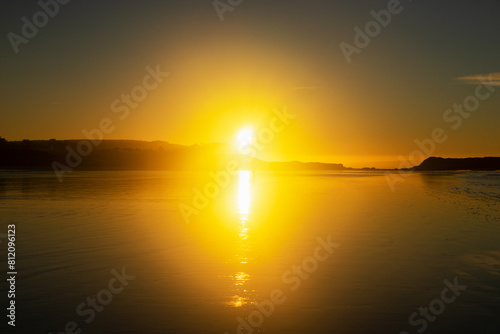 Sous un ciel teinté de jaune par le soleil levant, la plage de l'Aber sur la presqu'île de Crozon se transforme en un tableau vivant de reflets chatoyants, capturant la magie de l'aube. photo